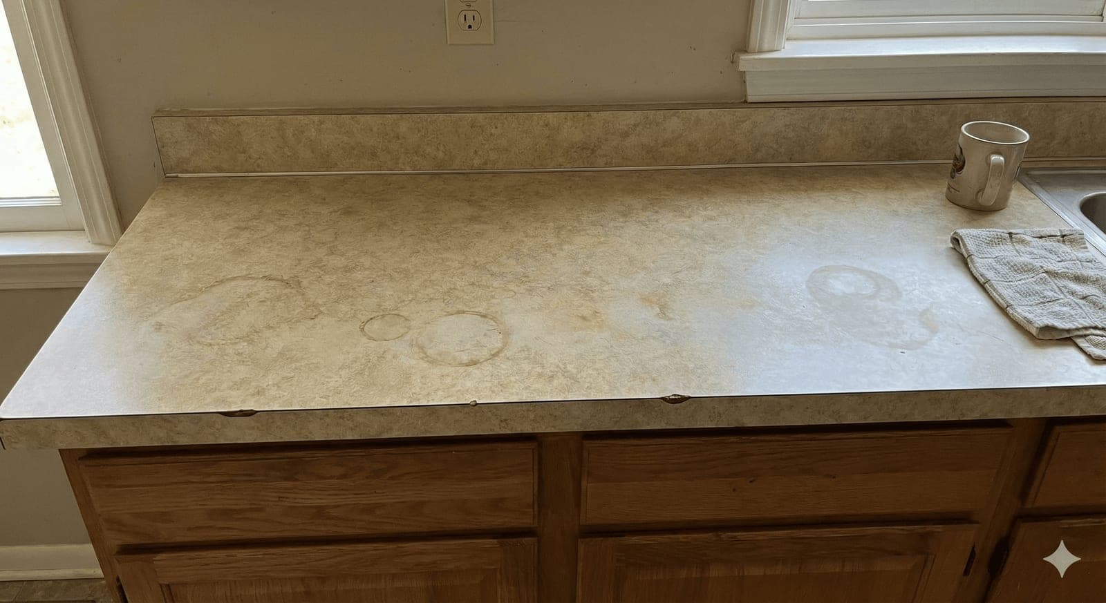 Kitchen countertop before refinishing — stained, dated laminate with water rings